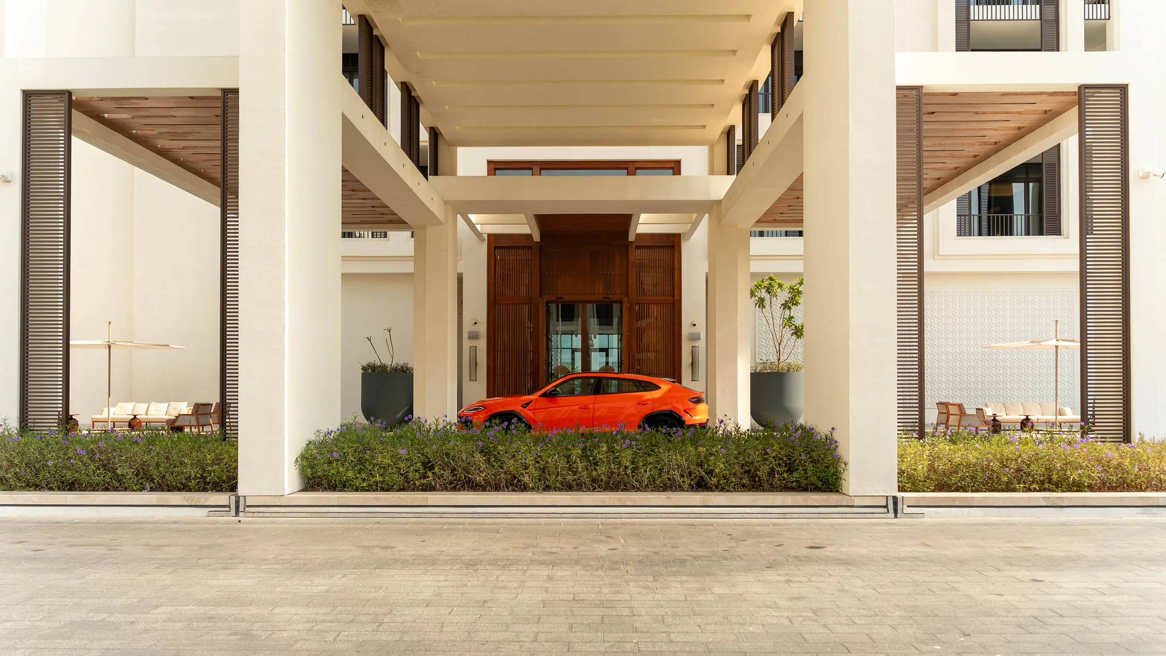 Orange Lamborghini Urus parked at a symmetric luxury hotel entrance in Muscat