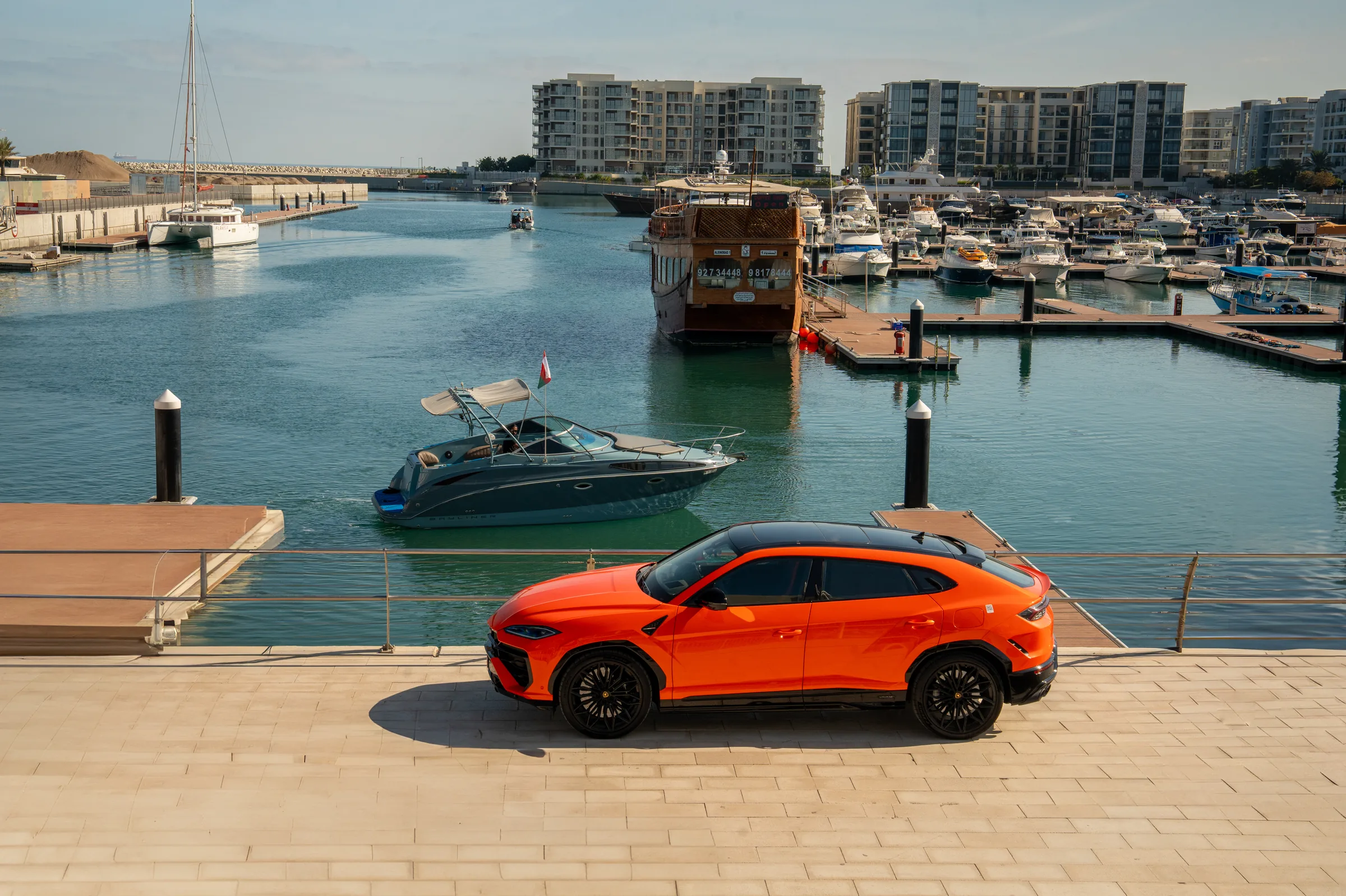 Lamborghini Urus side profile at Al Mouj Marina with yachts and waterfront buildings