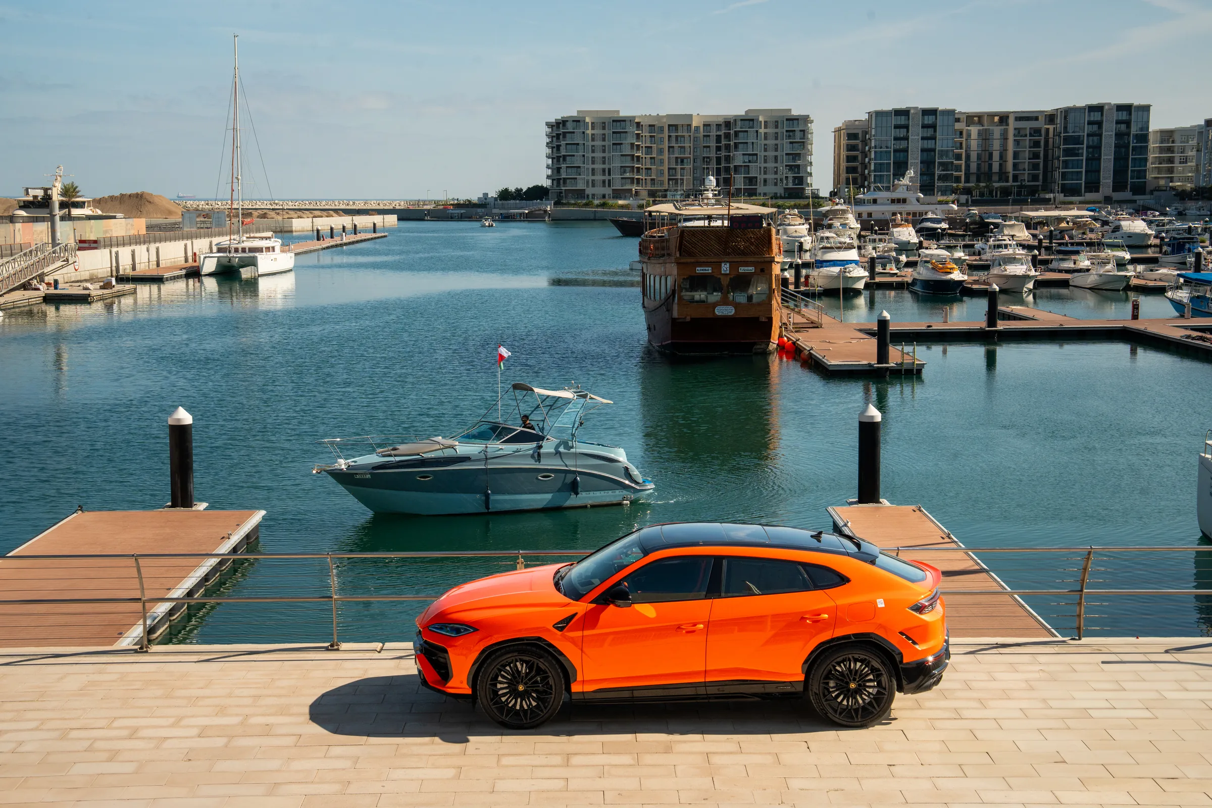 Wide view of Lamborghini Urus at marina with waterfront apartments